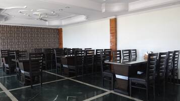 A dining area with a long table and multiple chairs, a patterned curtain, a ceiling fan, and a brick column.