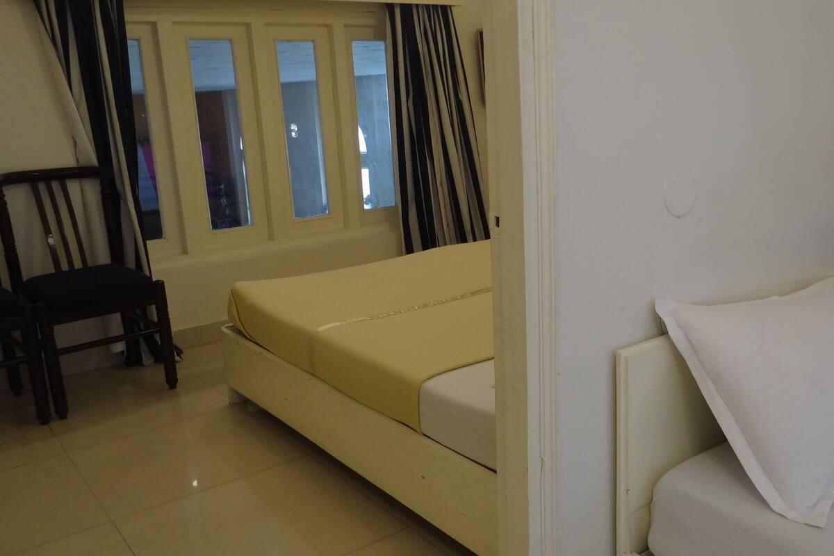 A room with a bed, a chair, a sofa, and a window with curtains.