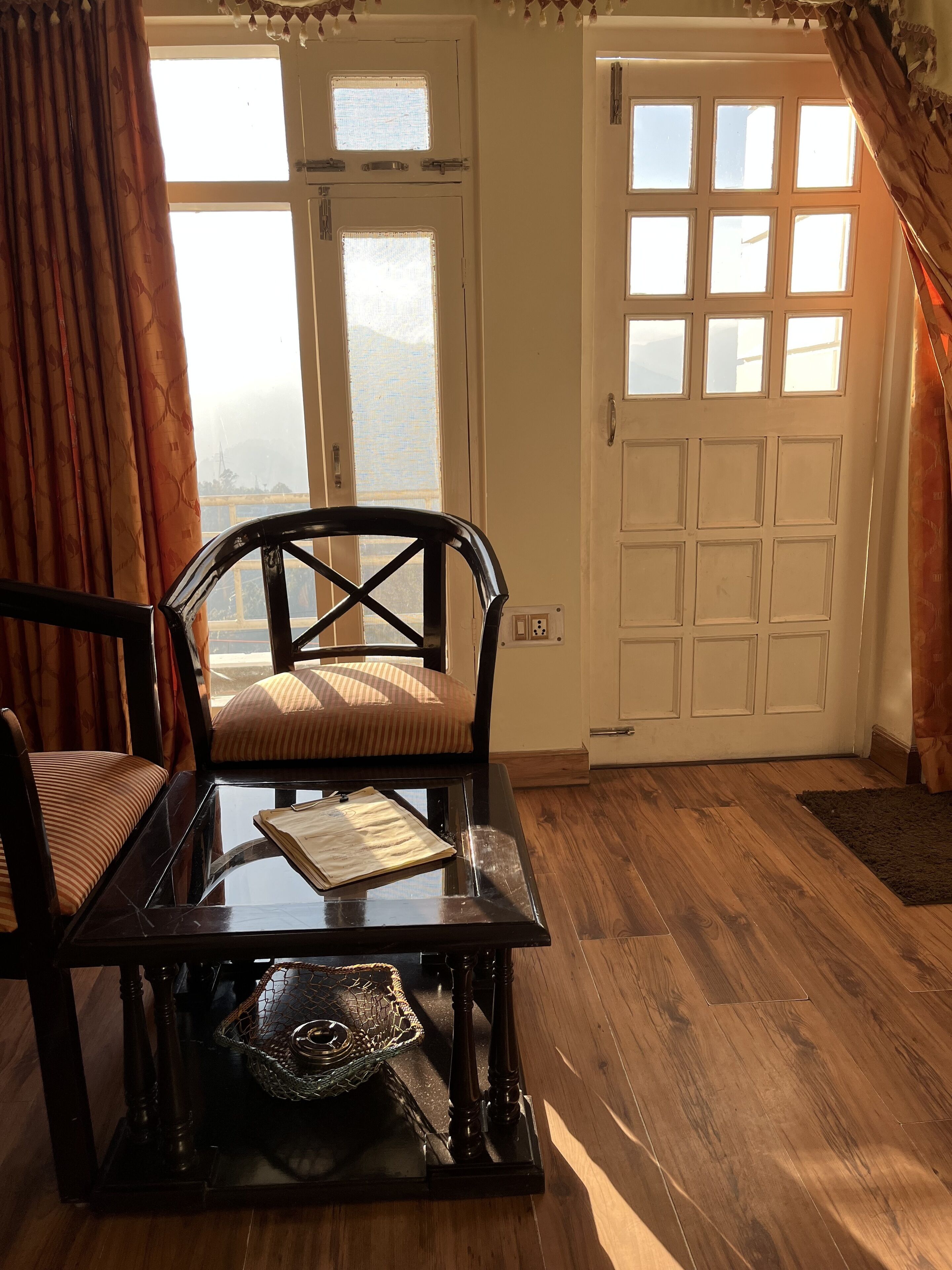 A room with a wooden floor, a black table with a book and a decorative basket, a striped cushion, and a chair.