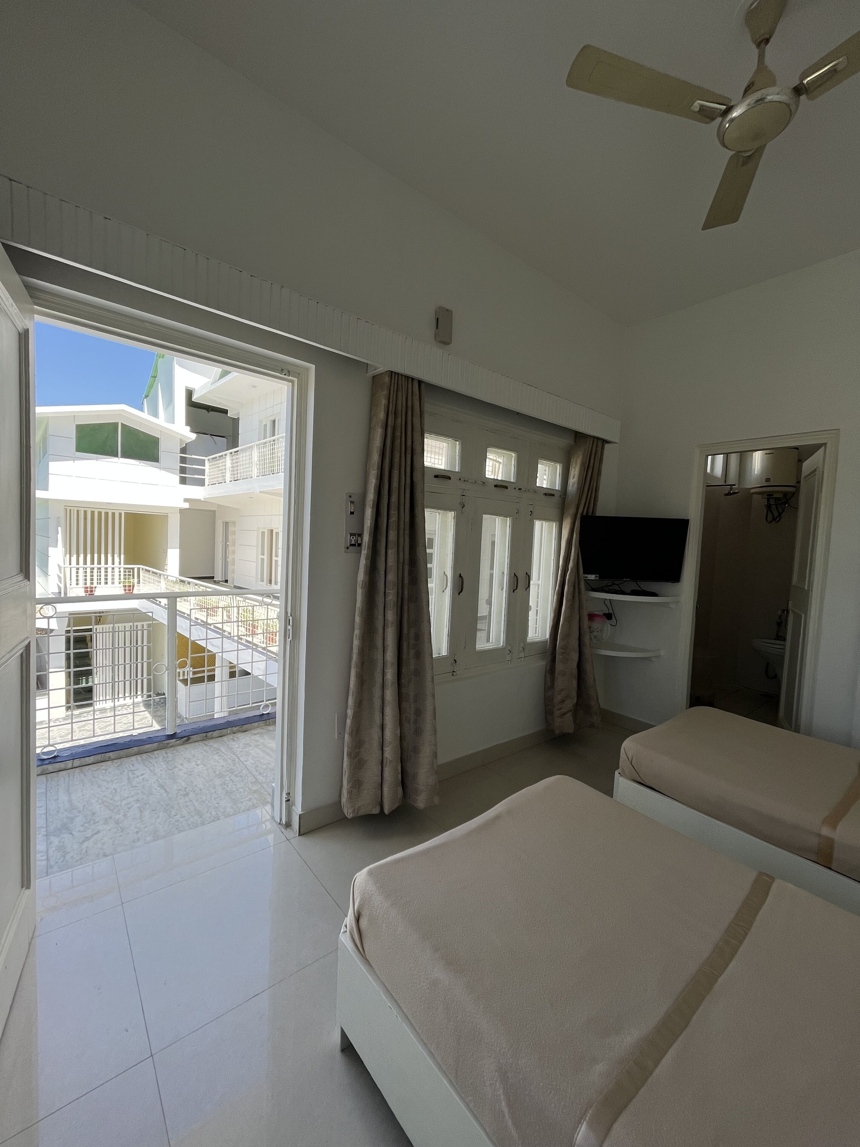 Una habitación de hotel con balcón, ventilador de techo, televisión y baño.