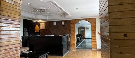 Eine Lobby mit Holzwandverkleidung, einer Rezeption, einer Sitzecke und Blick in einen weiteren Raum.