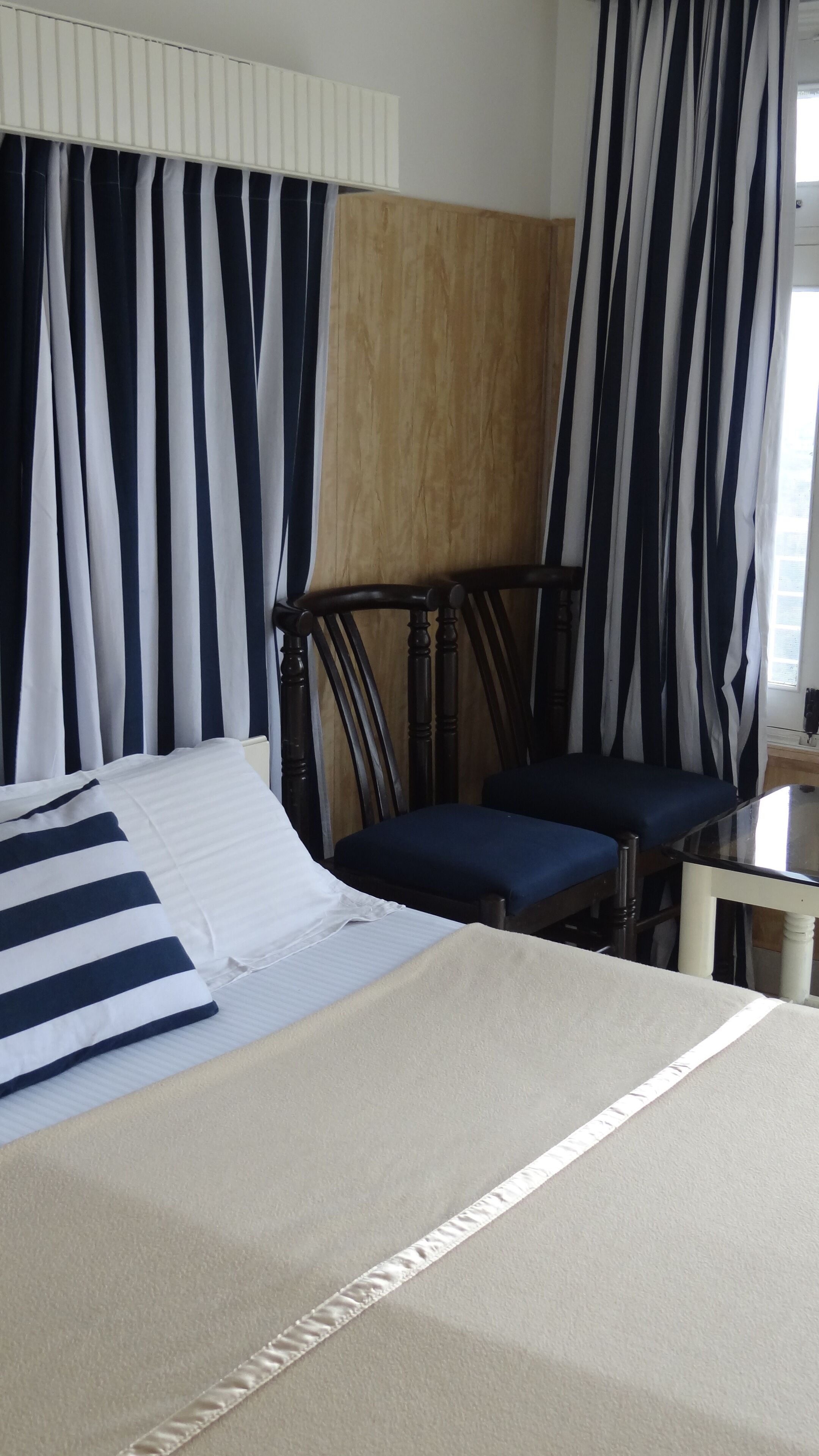 A hotel room with a bed, a wooden headboard, a chair, and striped curtains.