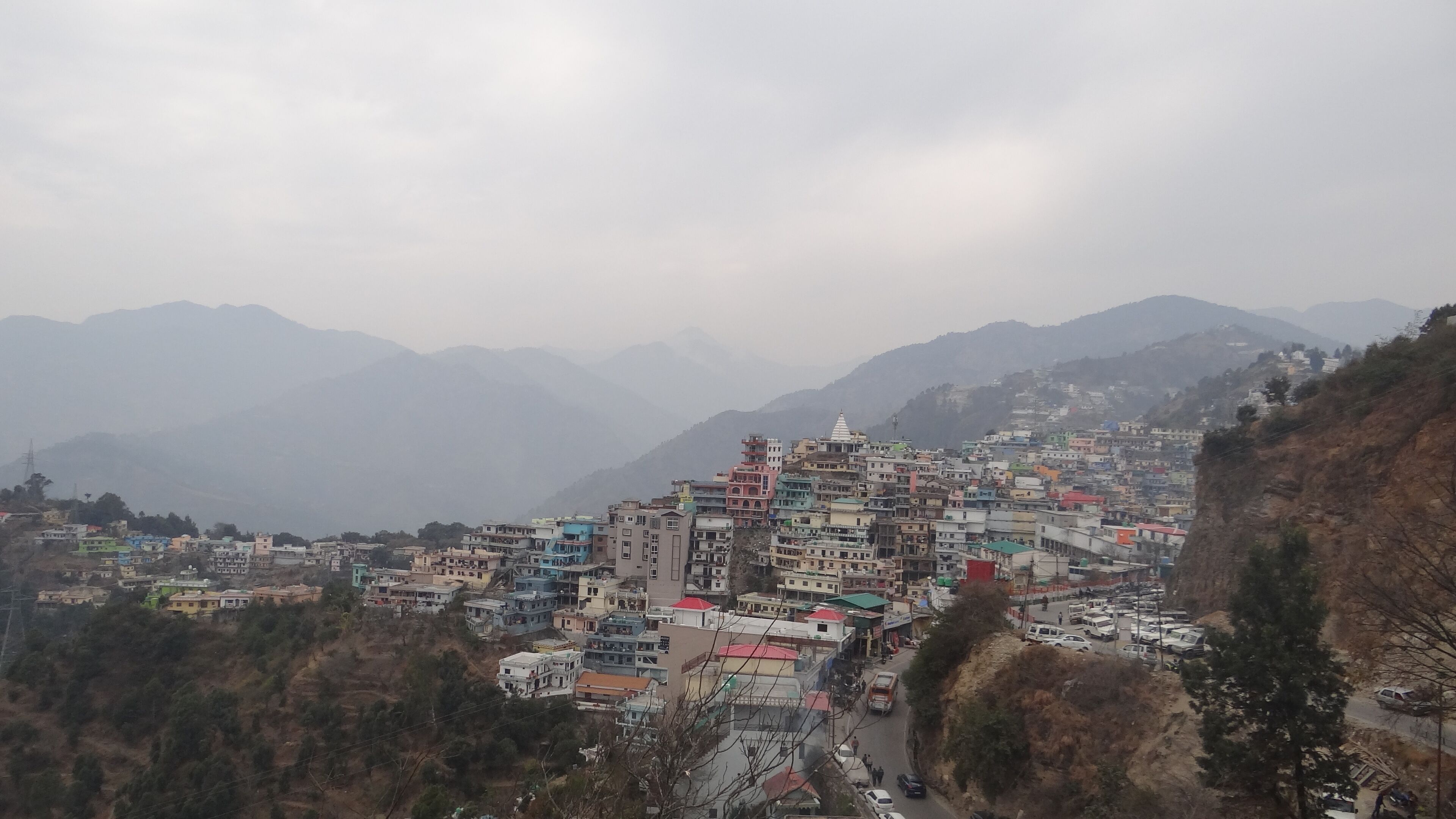 Un pueblo en una ladera con construcciones de varios pisos, un templo destacado y una carretera con vehículos.