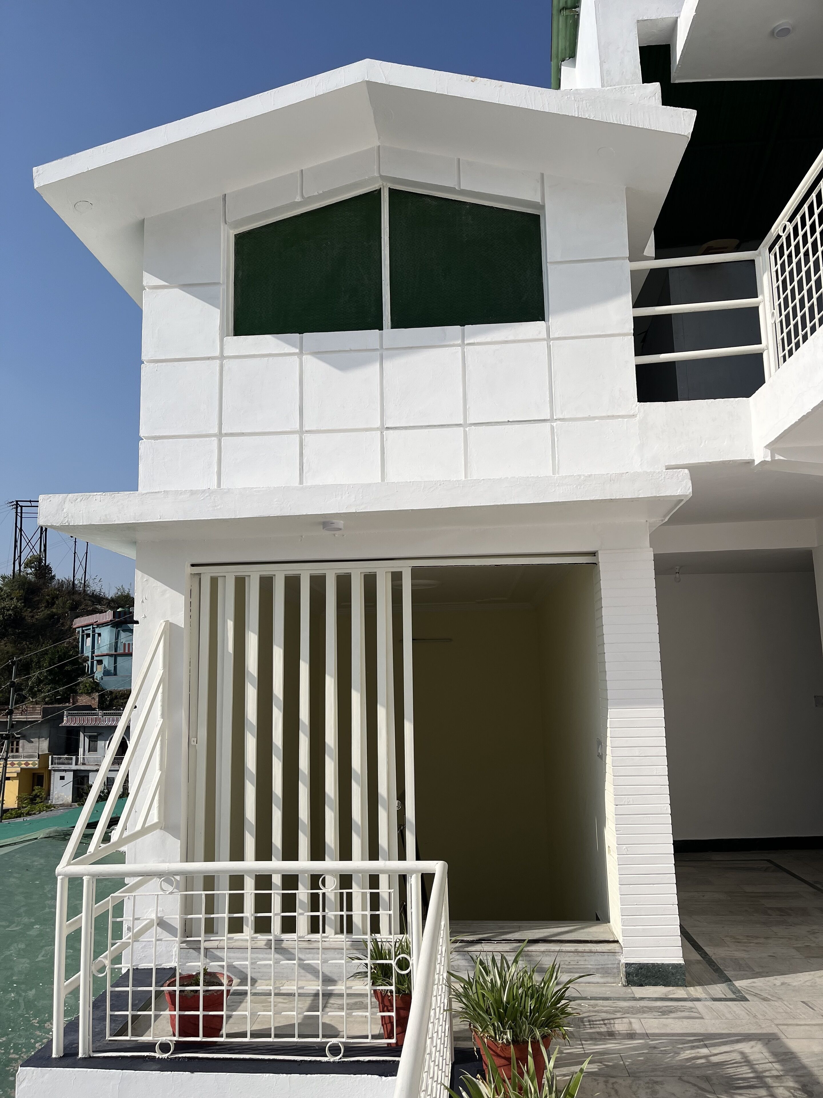 A modern two-story building with a white exterior, a balcony with a white railing, and a large window on the upper floor.