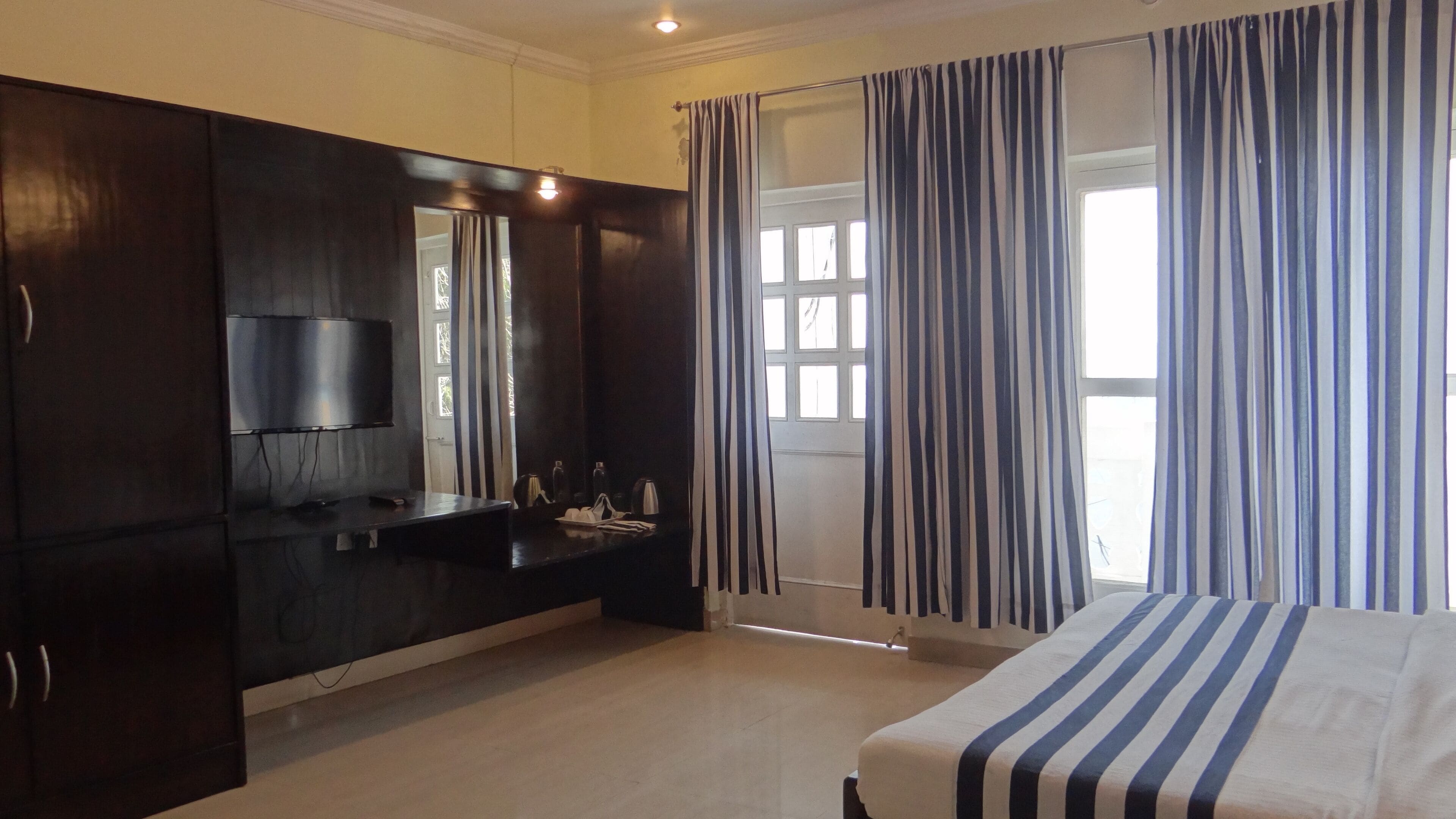 Un dormitorio con una cama, un televisor, un armario de madera oscura, un lavabo y una ventana con cortinas a rayas.