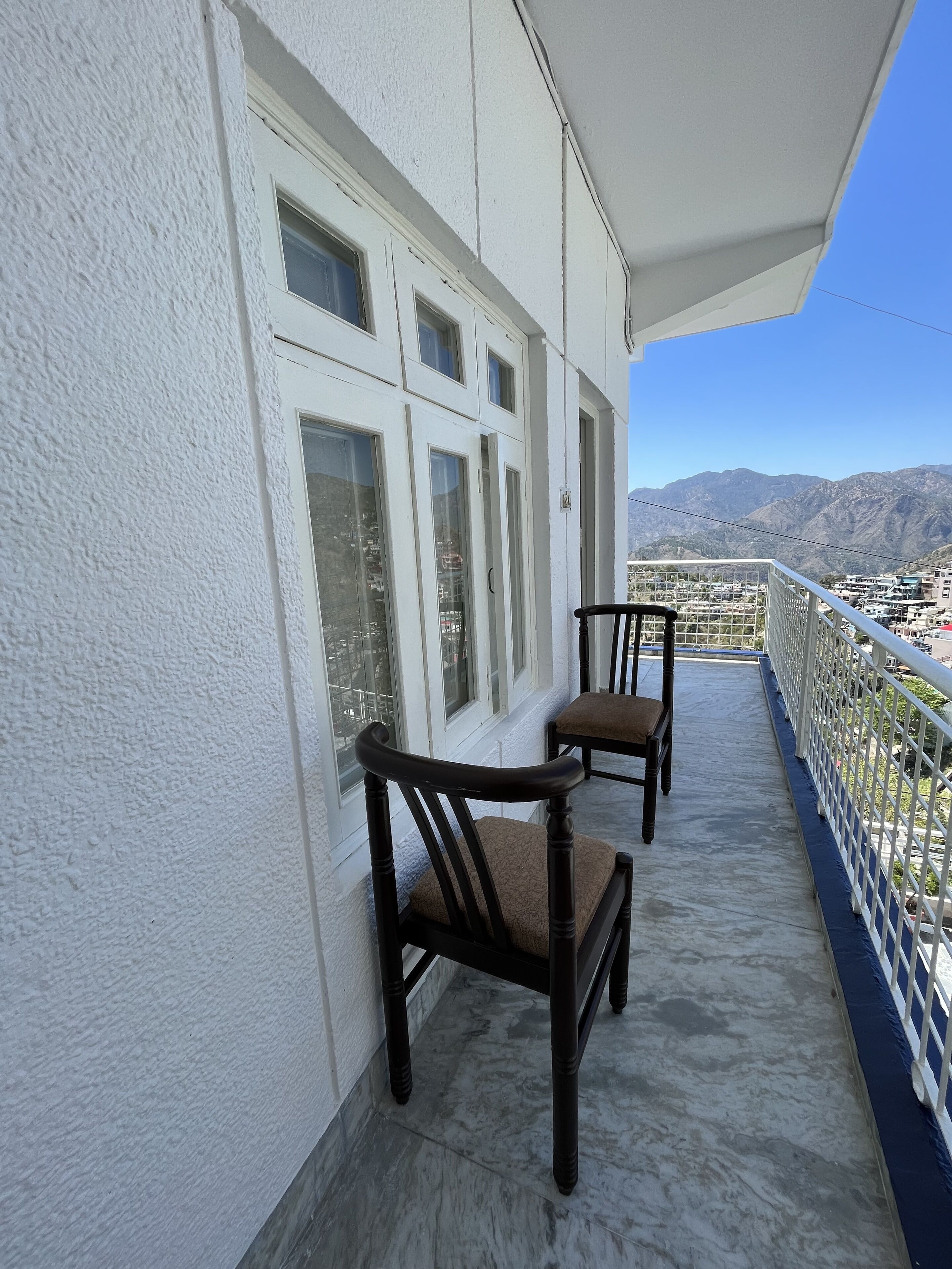 A balcony with two wooden chairs and a white railing, overlooking a mountainous landscape.