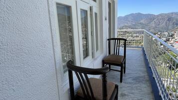 A balcony with two wooden chairs and a white railing, overlooking a mountainous landscape.