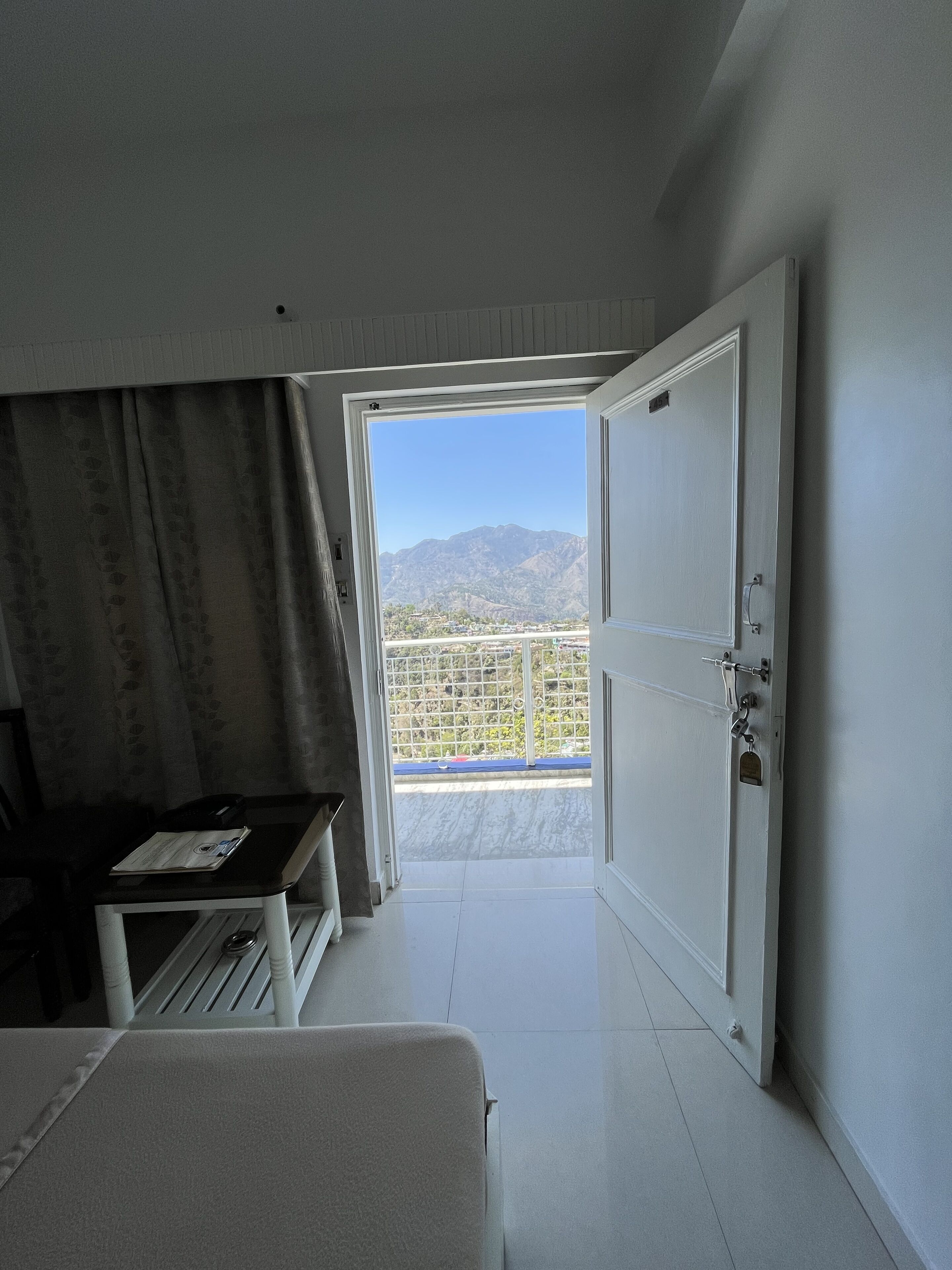 A room with a large open door leading to a balcony with a mountain view.