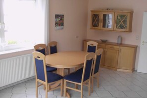 Uma sala de jantar com mesa redonda e quatro cadeiras, um armário com portas de vidro e uma janela com persianas.