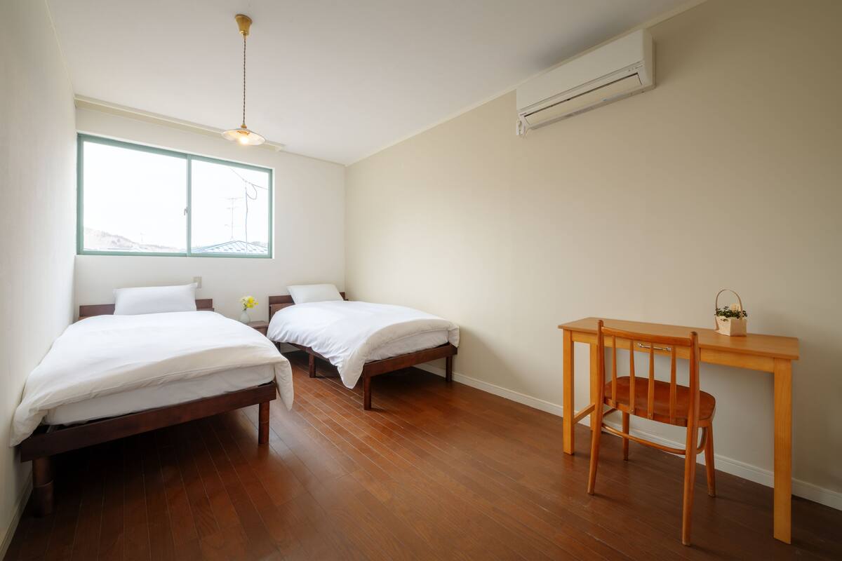 A room with two single beds, a wooden desk, and a chair.