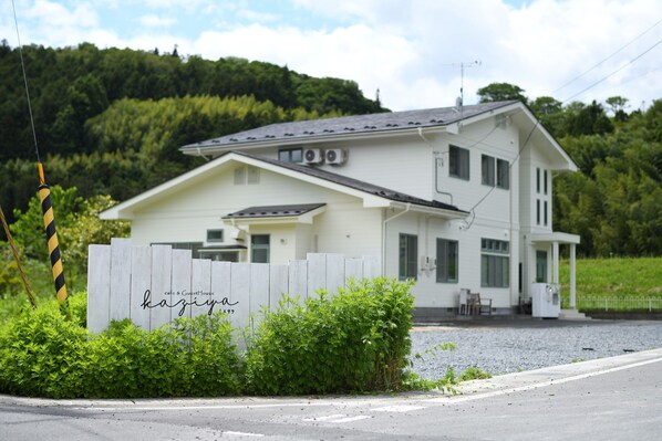 Un bâtiment à deux étages, à l’extérieur blanc, avec une clôture en bois portant une enseigne et une allée gravillonnée.