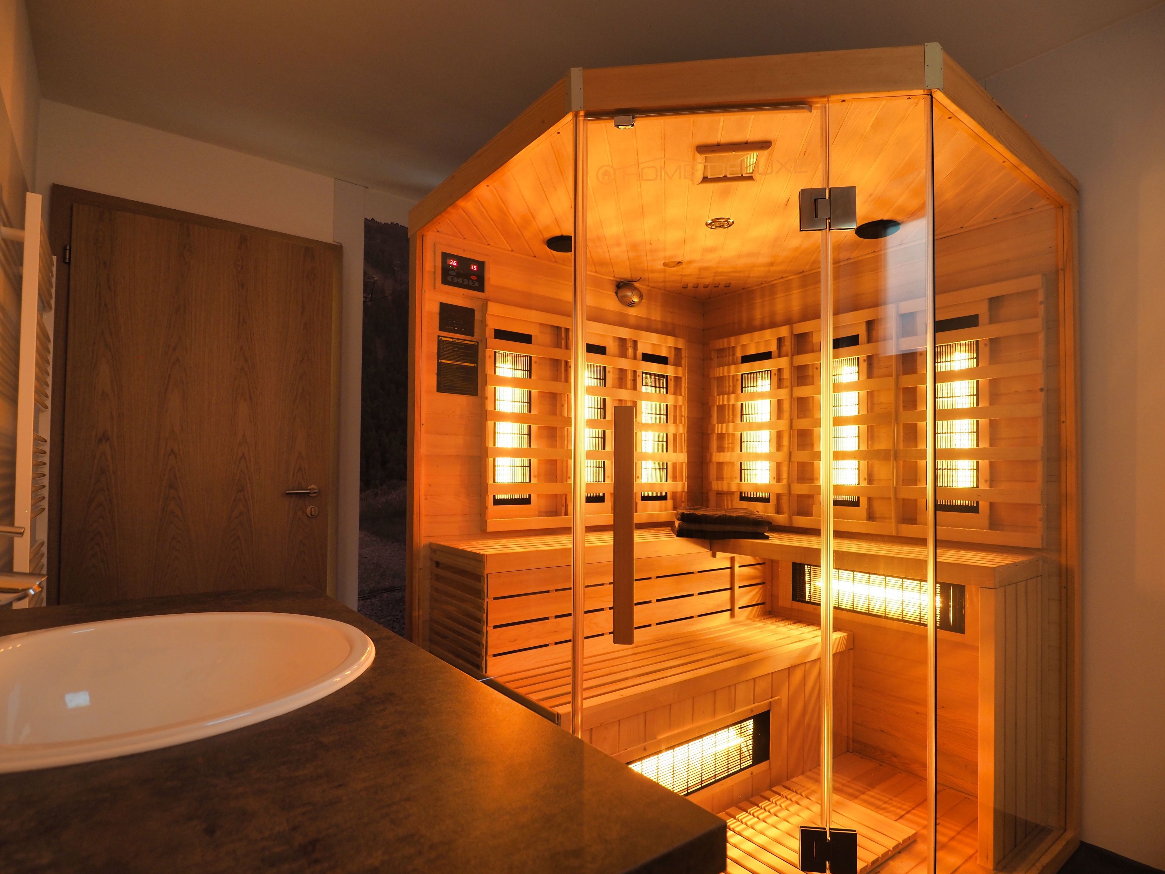 Un cuarto de sauna con bancos de madera y una pared de vidrio, una puerta de madera y un lavabo blanco.