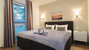 Moderni hotellihuone, jossa on suuri sänky, yöpöytä, seinään kiinnitetty lamppu ja ikkuna, jossa on verhot.