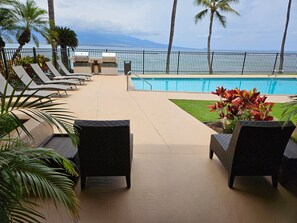 A poolside area with lounge chairs, a pool, and a view of the ocean.
