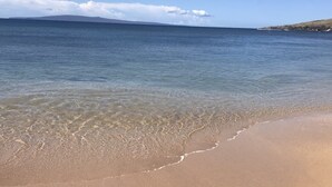 Une plage à l’eau claire, un rivage sablonneux et une montagne qui se dessine à l’horizon.