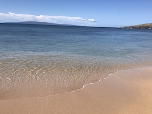 Una playa con agua cristalina, una orilla arenosa y una montaña a lo lejos.