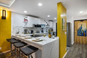 Una cocina moderna con una isla de mármol, taburetes de bar y un refrigerador.