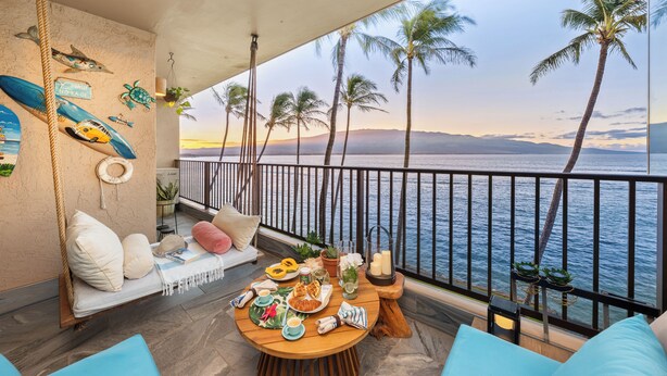 Un balcon avec vue sur la mer, une table en bois avec des éléments pour le petit-déjeuner, une plante suspendue et une pancarte de bienvenue.