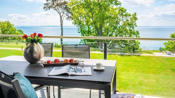 A balcony with a table set for a meal, a vase with flowers, and a view of the sea.