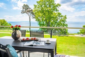 Un balcón con una mesa dispuesta para comer, un florero con flores y vista al mar.
