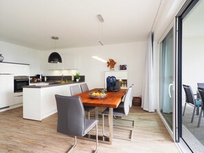 Une cuisine moderne avec des meubles blancs, un îlot central et un coin repas comprenant une table et des chaises en bois.