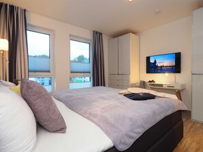 Une chambre d’hôtel moderne équipée d’un grand lit, d’un bureau avec un ordinateur, d’une télévision et d’une armoire.