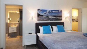 A modern bedroom with a bed, bedside tables, a nightstand, a mirror, and a painting of a beach scene.