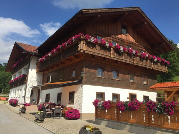 Un chalet traditionnel en bois, doté de balcons ornés de fleurs, d’un espace extérieur aménagé et surplombant un ciel dégagé.