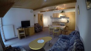 Una sala de estar acogedora con un sofá, un televisor y una mesita. Hay una zona de cocina con armarios y una estufa.