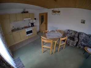 A compact kitchen with wooden cabinets, a microwave, and a stove. There is a dining table with chairs and a sofa.