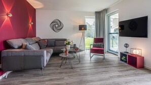 A modern living room with a grey sofa, a red armchair, a round coffee table with a vase of flowers, and a floor lamp. - Apartment Mohnblume - Oasis on the lagoon - Mohnblume (5-3) (Garz/Usedom)