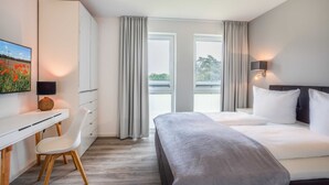 A modern hotel room with a bed, a desk, a chair, and a painting on the wall. - Apartment Mohnblume - Oasis on the lagoon - Mohnblume (5-3) (Garz/Usedom)