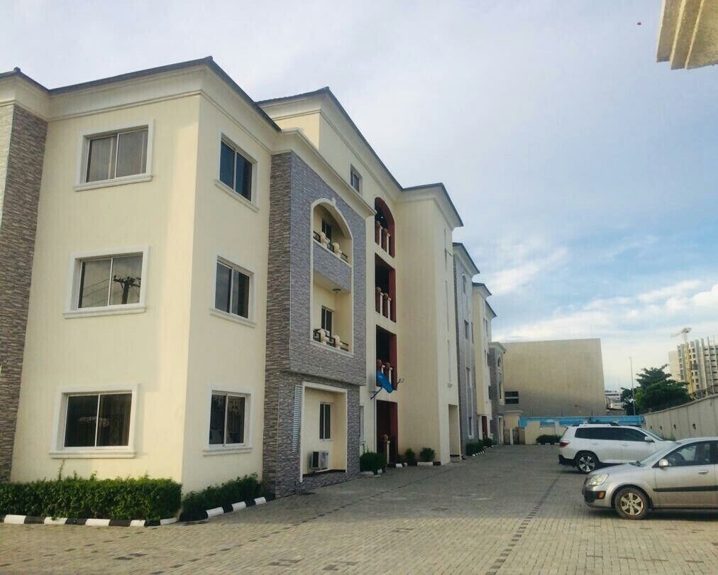 Un immeuble résidentiel à plusieurs étages, doté d’un toit plat, de nombreux balcons et d’une allée pavée.