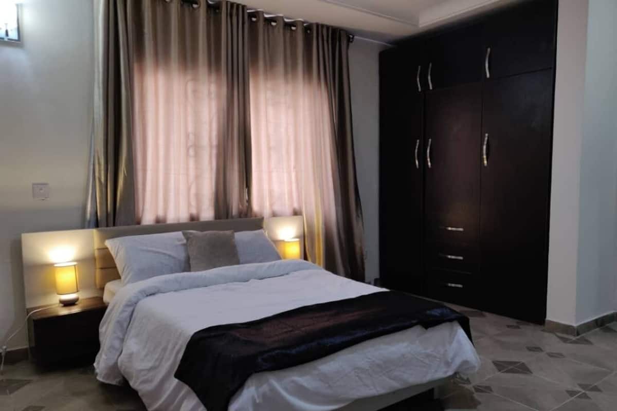 A bedroom with a bed, nightstands, a wardrobe, and curtains.