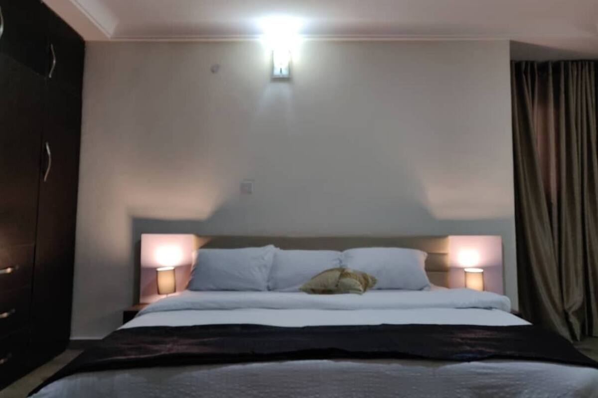 A hotel room with a bed, two bedside lamps, a headboard, and a wardrobe.