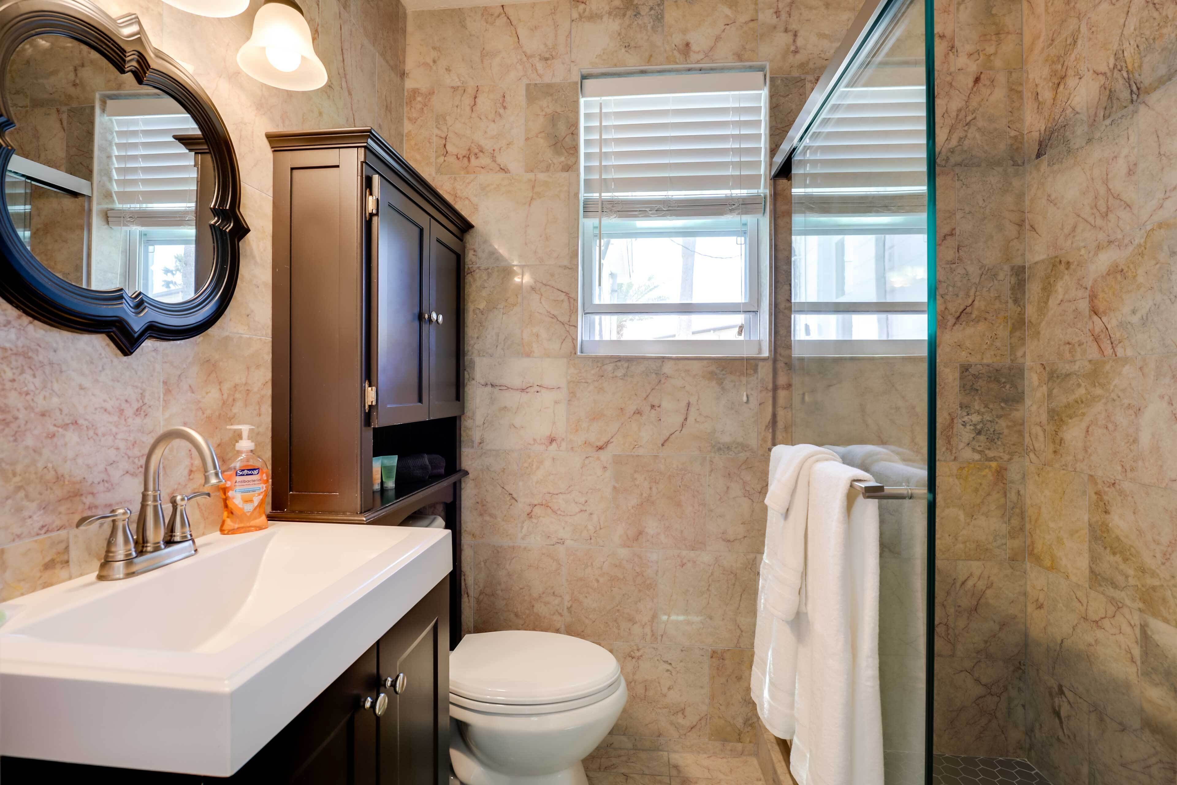 Une salle de bain avec un mur en marbre, un lavabo blanc, un meuble sombre, des toilettes et une cabine de douche en verre.