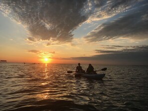 A sunset over a calm sea with kayaks and a distant pier.
