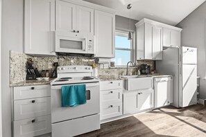 A modern kitchen with white cabinets, a granite countertop, a stainless steel range hood, and a built-in microwave.