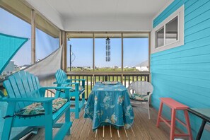 A covered porch with turquoise chairs, a table with a floral tablecloth, and a view of the landscape.