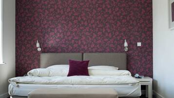 A neatly made bed with a headboard, a bedside table with a lamp, and a wall with a floral pattern.
