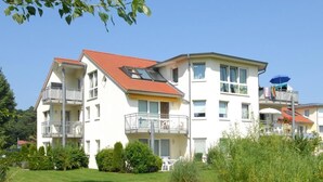 A multi-story residential building with balconies, a garden area, and a clear sky.