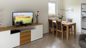 A modern living room with a flat-screen TV, wooden dining table, and chairs.