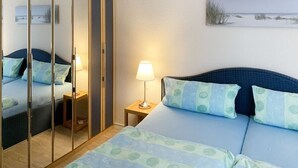 A bedroom with a bed, a nightstand, a lamp, a wardrobe, and a wall-mounted artwork.