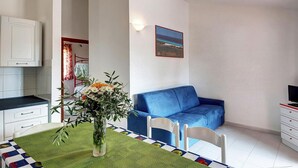 A compact living space with a dining area, a blue sofa, a small kitchen, and a framed picture on the wall. - Apartment in San Teodoro (San Teodoro (SS))