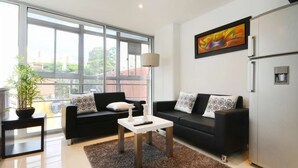 A modern living room with a black sofa, a white coffee table, and a large window offering a view of the city. - Two Bedroom Middle of Park lleras AC, Hot tub Bars downstairs (Medellin)
