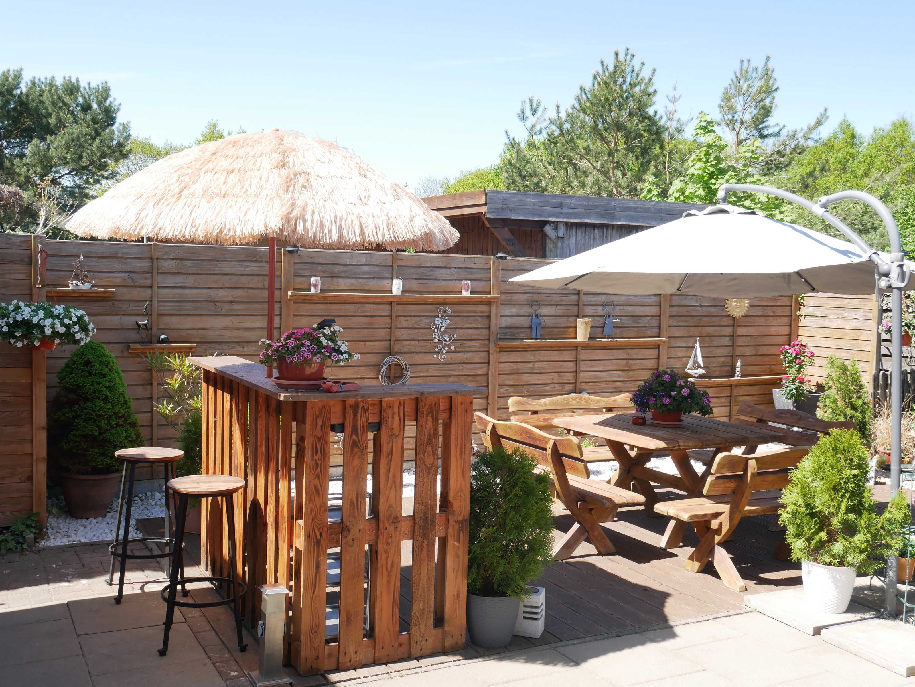 Eine Terrasse im Freien mit Holzmöbeln, einem Reetdachschirm und Topfpflanzen.