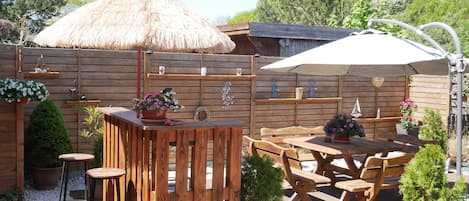 An outdoor patio with wooden furniture, a thatched umbrella, and potted plants.