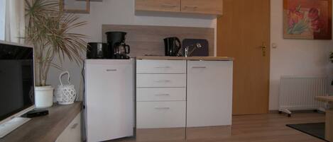 A compact kitchen with a white refrigerator, a coffee maker, and a potted plant.