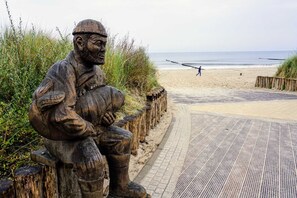 A wooden bench sculpture on a beach path with a view of the ocean and a person in the distance. - Bungalow Vincent, with terrace, barbecue & WLAN - Bungalow with garden, terrace and (Zempin)