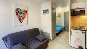 Un espacio habitable pequeño con sofá, una obra de arte con forma de corazón, una kitchenette con microondas y una cama al fondo.